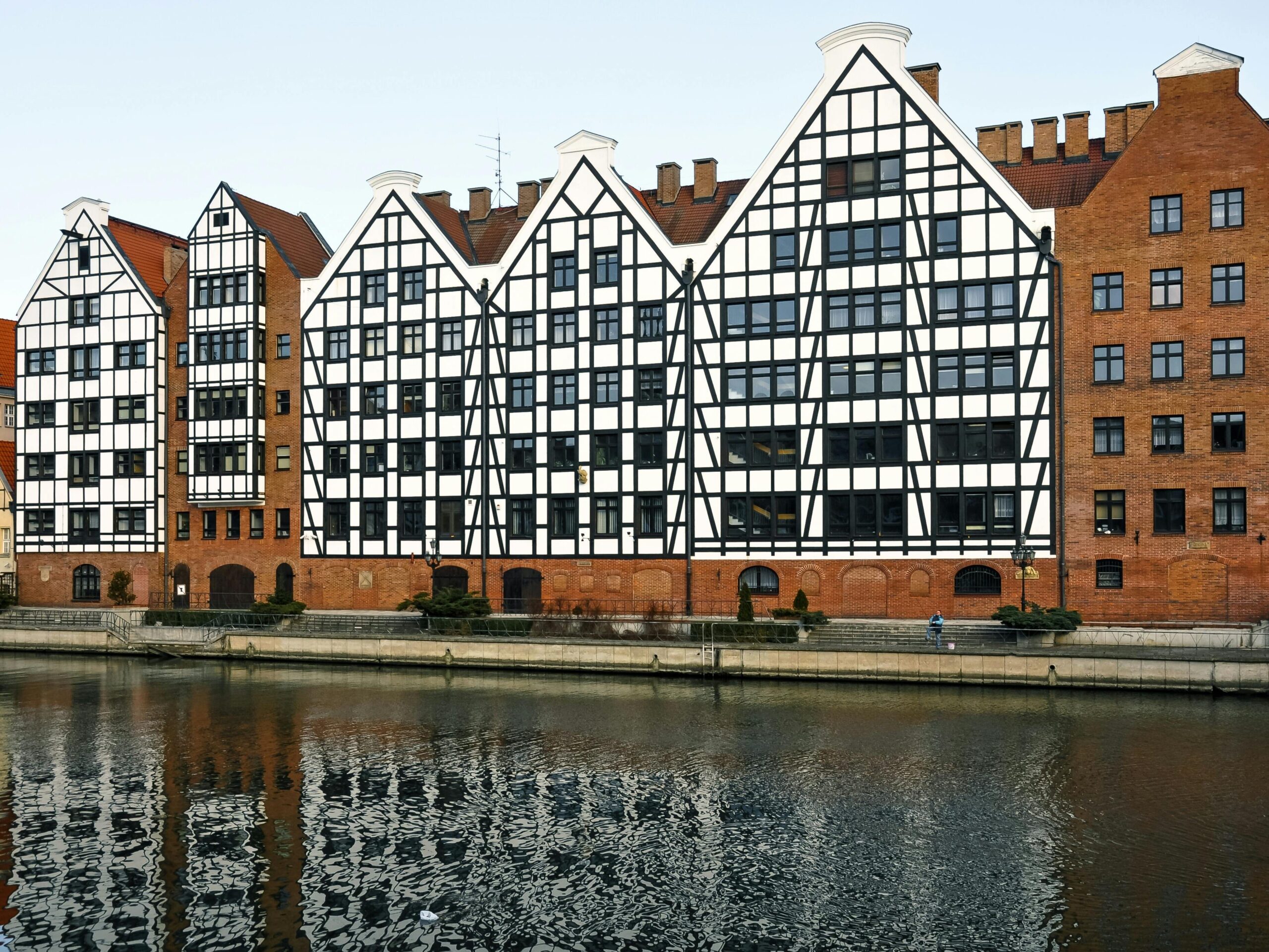 Idyllic riverfront view in Gdańsk, showcasing historic architecture reflecting in calm waters.