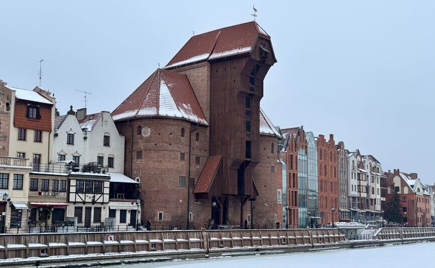 The iconic Gdansk Crane, a historic landmark, covered in winter snow along the river.